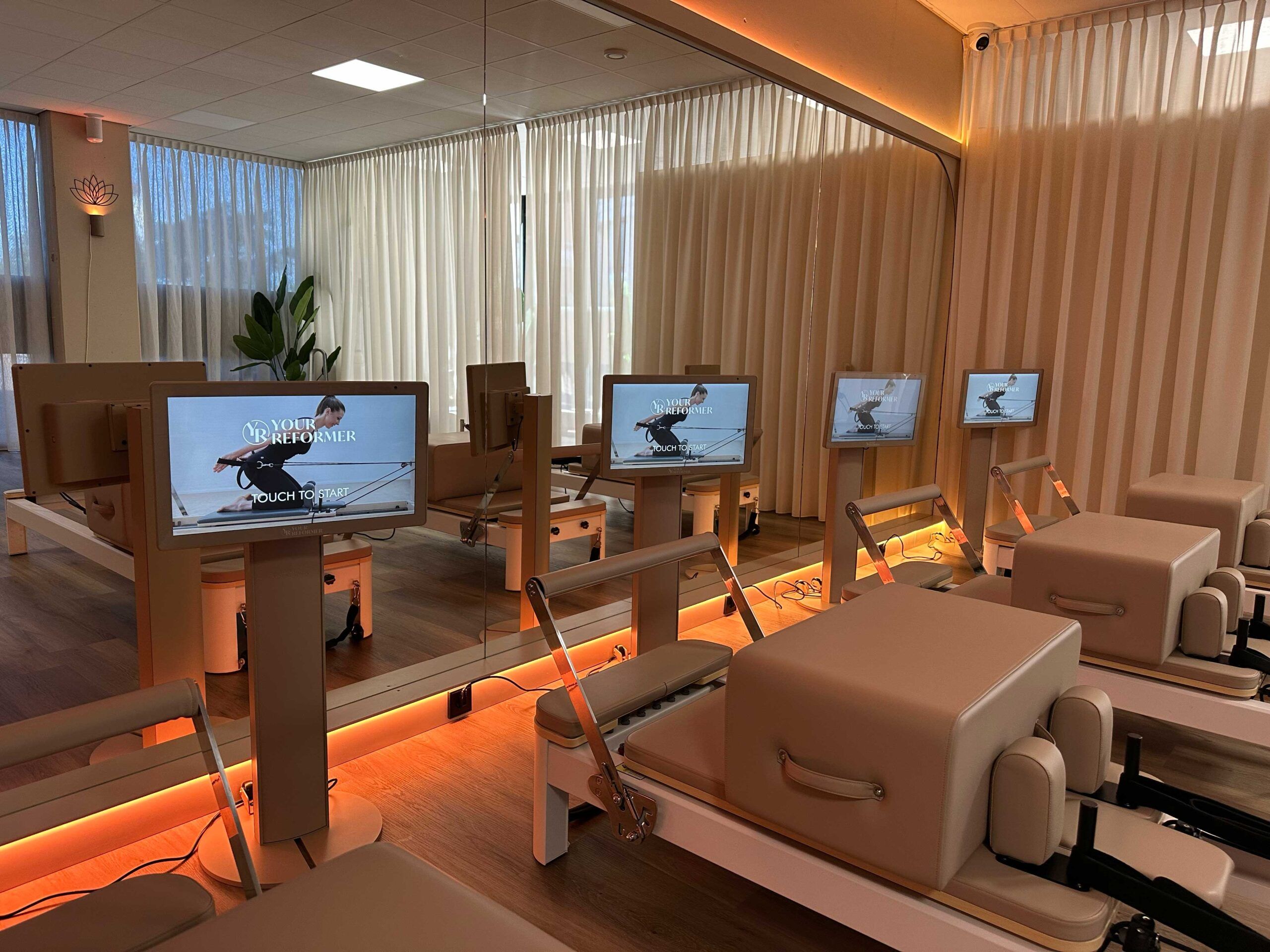 De reformerzaal van MOOON in warm licht, met een scherm bij elke reformer